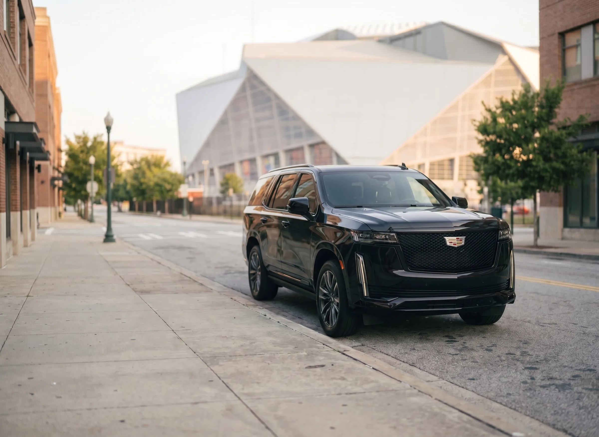 A black Cadillac Escalade parked at a downtown Atlanta curb in morning light, the exterior of Mercedes-Benz Stadium rising behind it.