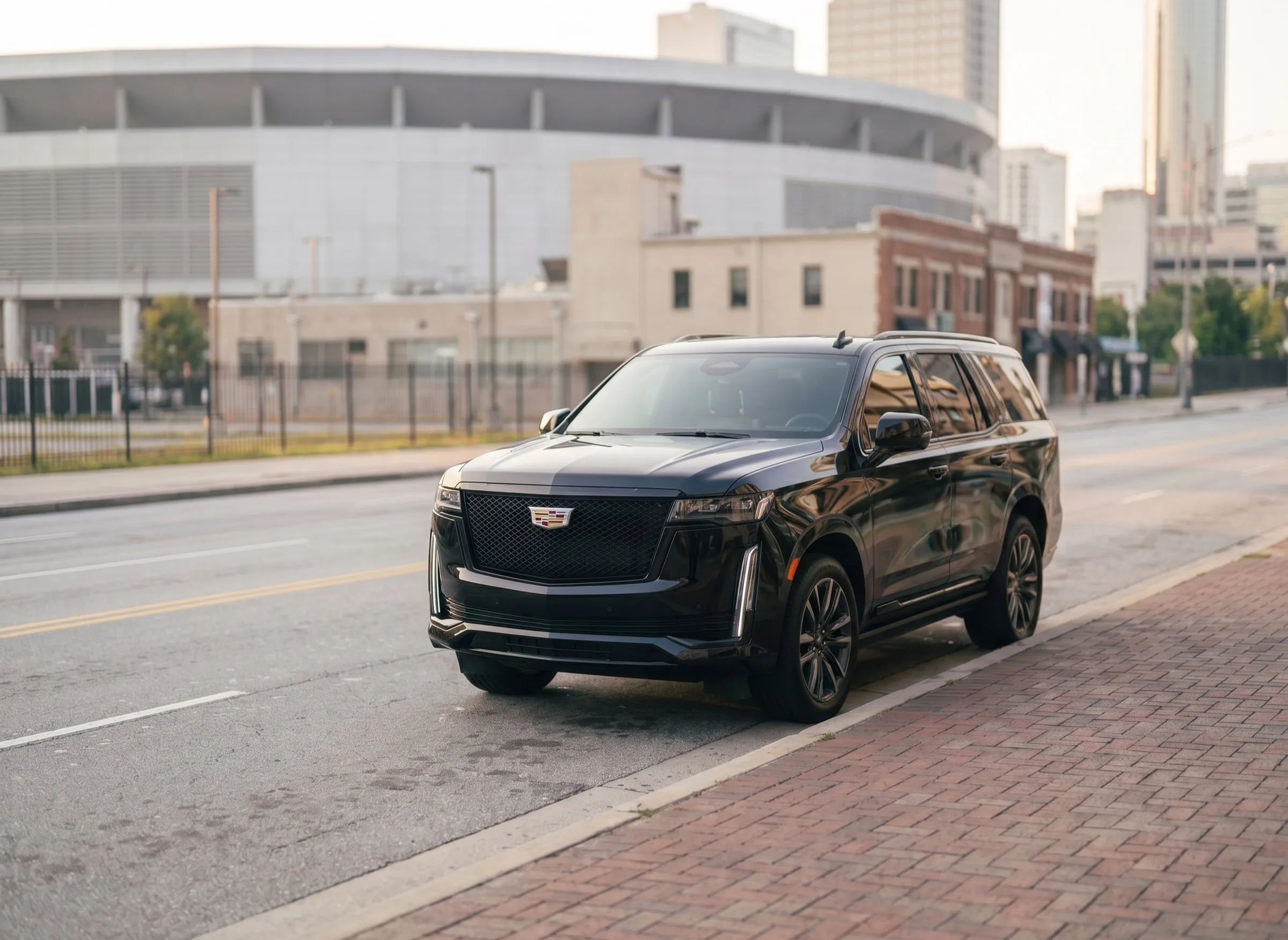 A black Cadillac Escalade parked along a downtown Atlanta curb near Mercedes-Benz Stadium in clear daylight.