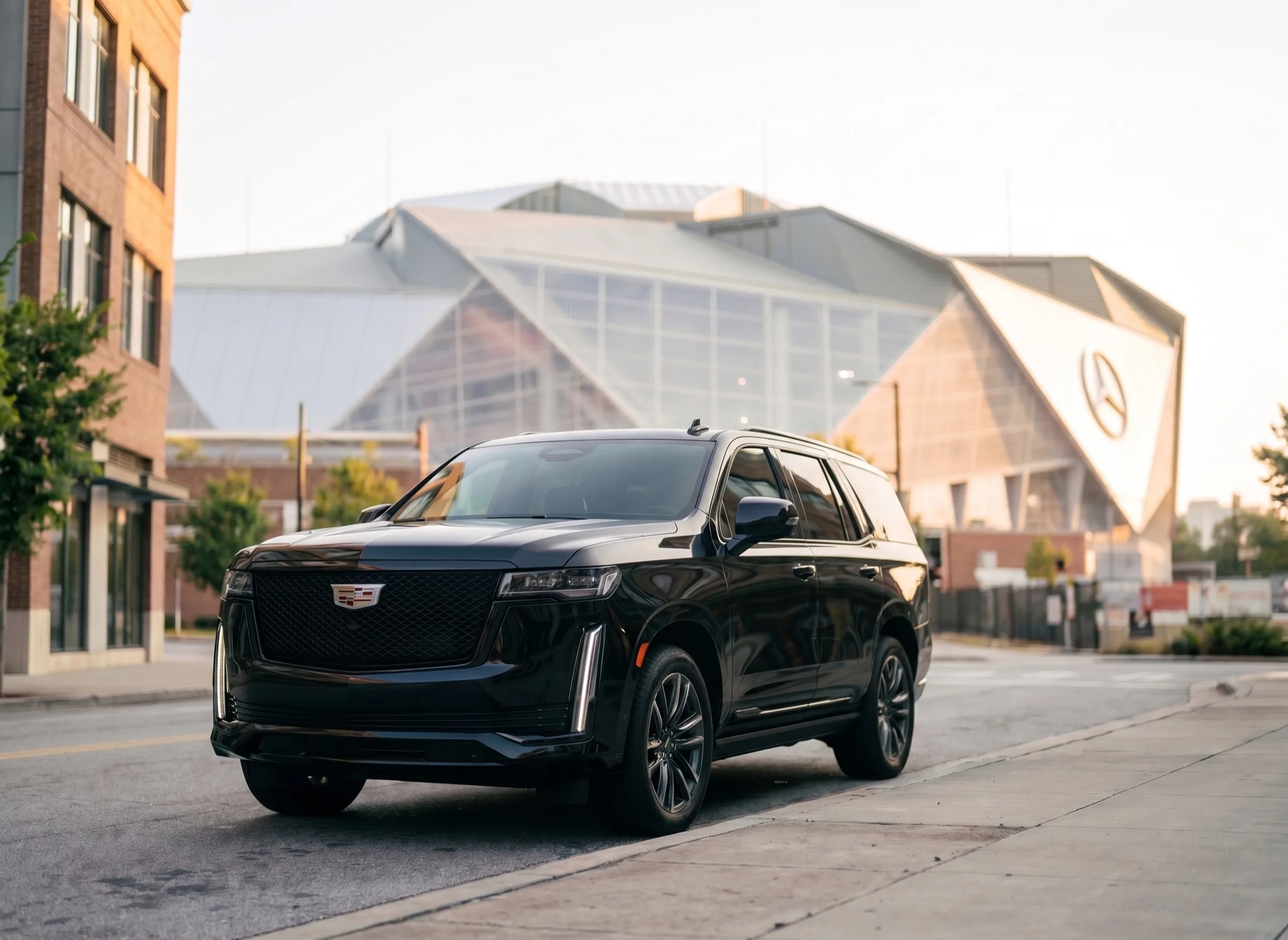 A black Cadillac Escalade parked at a downtown Atlanta curb, the exterior of Mercedes-Benz Stadium rising behind it in morning light.